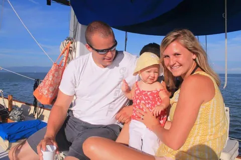 A family with their baby on deck, smiling, the bay behind