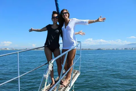 Two friends at the bow of a sailboat, arms open